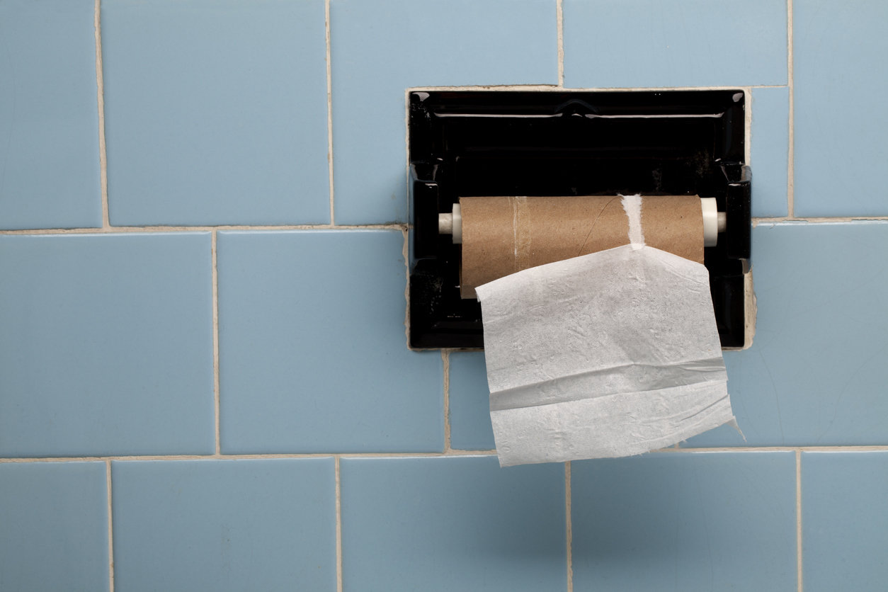 Last square of toilet paper on roll against blue tile wall